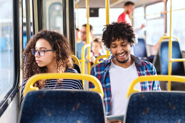 istock Two young persons sitting next to each other in city bus. Girl looking through window while guy having earphones on ears and using tablet. 1082102046