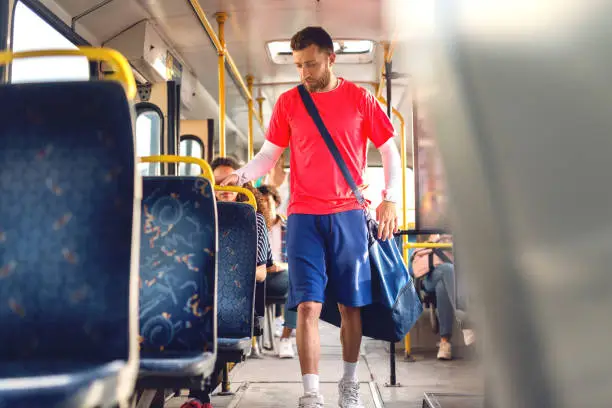 Photo of Young man taking sit in a bus, carrying sports bag.