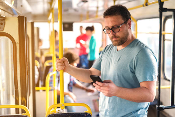 istock Middle-aged bearded man with eyeglasses using smart phone for reading or writing message while standing in city bus. 1082104138