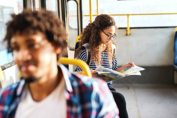 des jeunes femmes lisent un journal et s’assoient en attendant le départ du bus. technique de mise au point de l’image. - bus inside of people train photos et images de collection