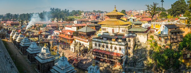 Crowds on the banks of the Bagamati River beside the iconic Hindu temples of Pashupatinath and the funeral ghats of the UNESCO World Heritage Site in the heart of Kathmandu, Nepal's vibrant capital city.