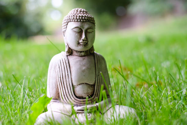 istock Small white Buddha statue in a meditation pose on green natural bright background. Religious symbol of buddhism 1082195732