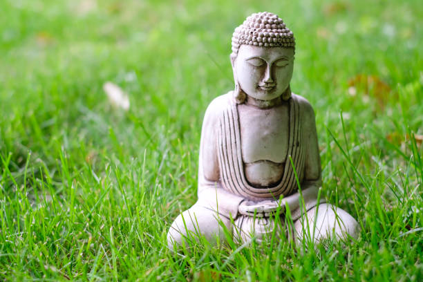 istock Small white Buddha statue in a meditation pose on green natural bright background. Religious symbol of buddhism 1082196830