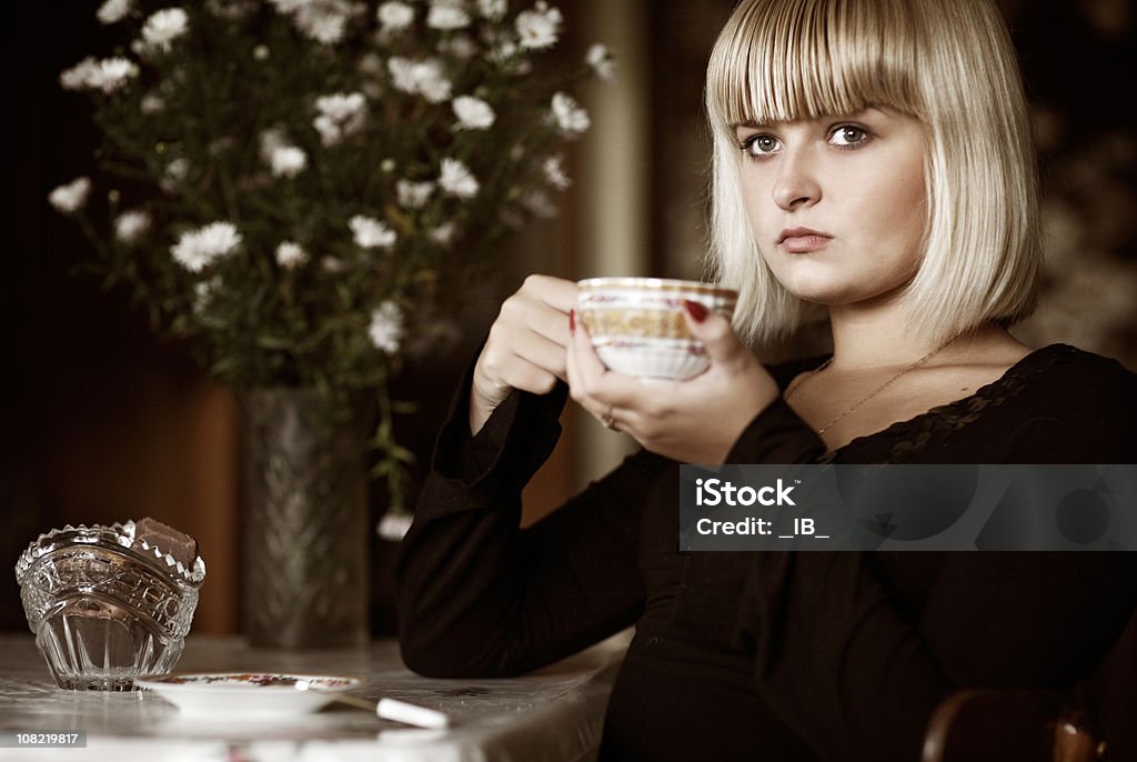 Young Woman Drinking Tea At Table With Flowers and Cookies  Adult Stock Photo