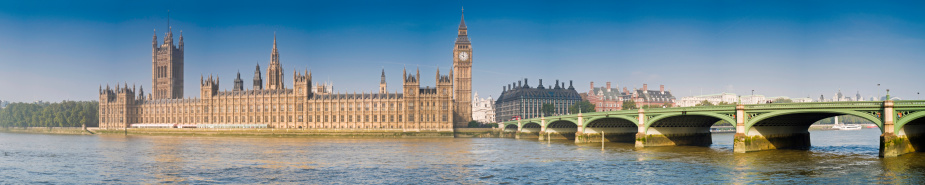 Panoramic view across the River Thames in central London to the gothic spires and iconic towers of the Palace of Westminster, seat of the British Government, Portcullis House, Whitehall and Westminster Bridge. ProPhoto RGB profile for maximum color fidelity and gamut.