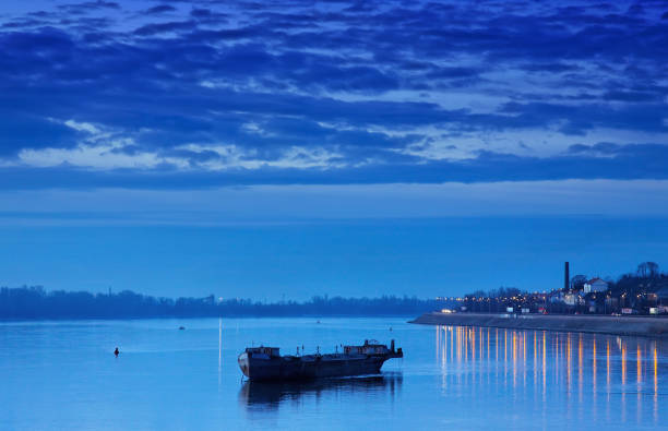 A tour boat shines with white and blue lights, moored at Bajo de Guia in Sanlucar de Barrameda, creating reflections on the dark Guadalquivir River.