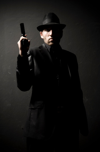 Portrait of a gangster in front of a black wall.
