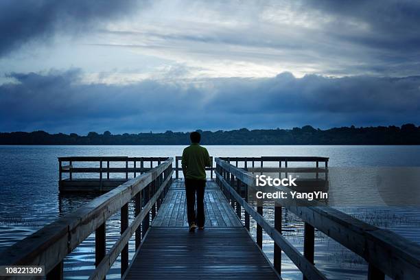 Photo libre de droit de Orageux Matin Avec Un Homme Marchant Sur Le Quai En Bois Sur Le Lac banque d'images et plus d'images libres de droit de Vue de dos