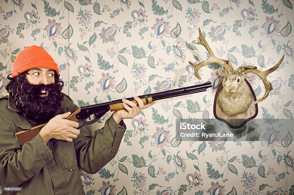 Crazy Hunter &amp; Jackalope A wild looking woodsman hunts taxidermy, a stuffed jackalope (rabbit with antlers).  Vintage wallpaper background, horizontal with copy space. Hunting Trophy Stock Photo