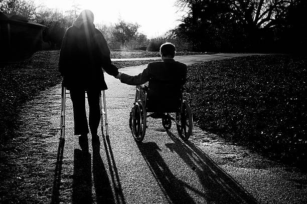 Asian elderly man pushing his wife in wheelchair at park. Senior couple enjoying leisurely stroll, surrounded by lush greenery. relaxation in public park of senior couple. copy space