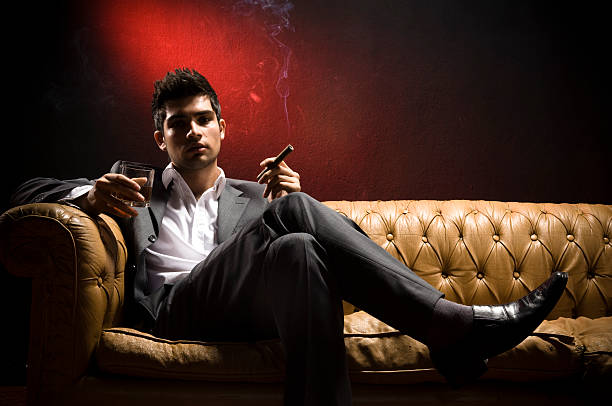 Attractive Young Man Jacket weared young man sitting on a cream leather seat and smoking. man cigar stock pictures, royalty-free photos & images