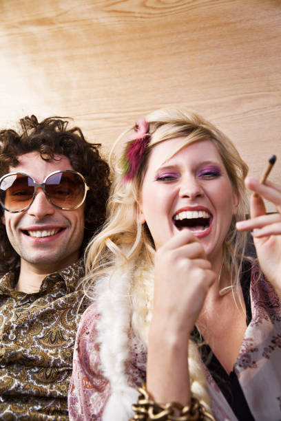 jeune femme riant avec hippie homme fumeur de cannabis - 1970s style women hippie retro revival photos et images de collection