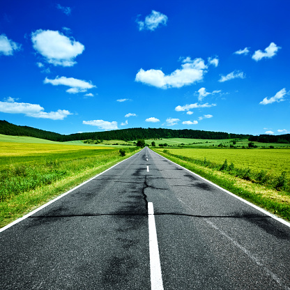 Country rural road,blue sky,clouds and green meadow and trees in summer landscape.