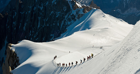 Intrepid Alpinists carefully negotiating the steep snow ridge from the Aiguille du Midi high on the Mont Blanc massif high in the to the glacial col of the Vall