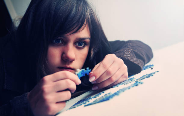 Young Woman Lying on Floor Putting Puzzle Pieces Together stock photo