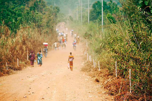 Karawa, Democratic Republic of Congo - August 24, 2013: An unpaved road in rural Congo, a lot of people are walking on the road which connects two villages in the province of Equateur. Walking and bicycling is nearly the only way of transportation in the poor regions of Congo. Mostly women are carrying heavy loads of goods on their heads when they are walking to a market place.