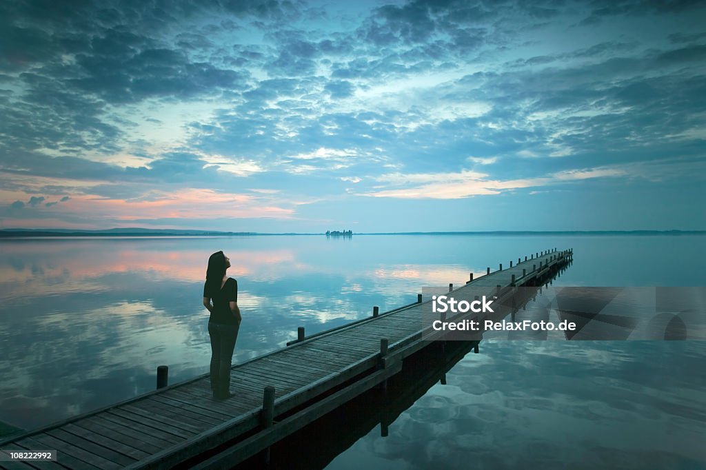 Silhouette di giovane donna in piedi sul Molo del lago al tramonto - Foto stock royalty-free di Donne