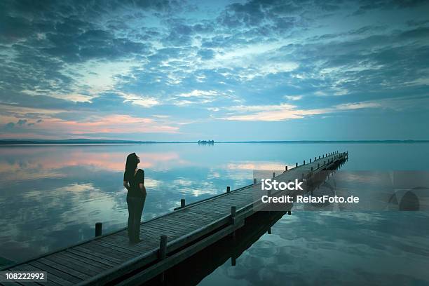 Silhouette Di Giovane Donna In Piedi Sul Molo Del Lago Al Tramonto - Fotografie stock e altre immagini di Donne