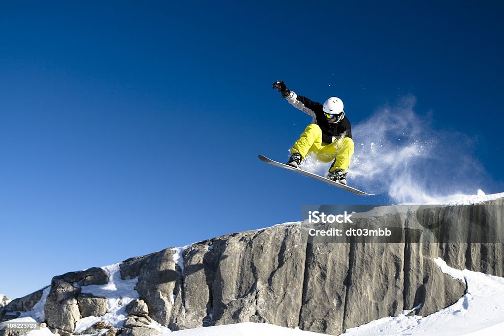 Snowboarder Dropping Off Short Cliff Against Blue Sky  Snowboarding Stock Photo