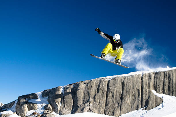 Snowboarder Dropping Off Short Cliff Against Blue Sky stock photo