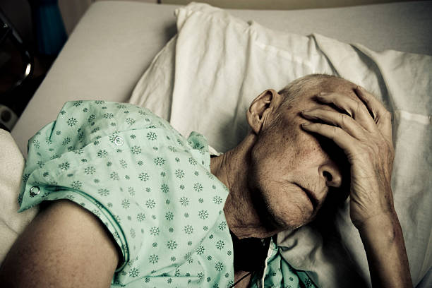 Sick and Senior Man Wearing Hospitable Gown Lying in Bed  cancer illness stock pictures, royalty-free photos & images