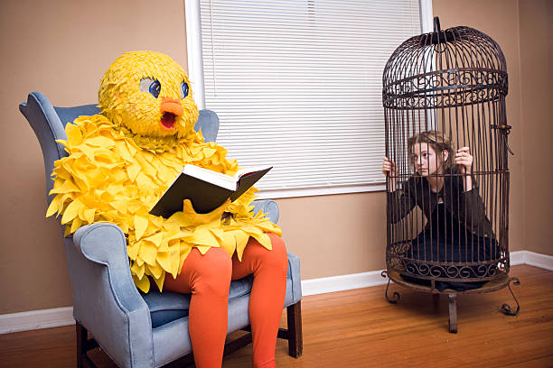 Large Bird Costume with Pet Person Something seems backwards here...young girl in a giant bird cage, big yellow canary relaxing with a good book and reading out loud. birdcage stock pictures, royalty-free photos & images