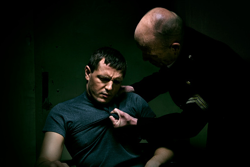 Policeman pulling the prisoner's t-shirt during the interrogation.