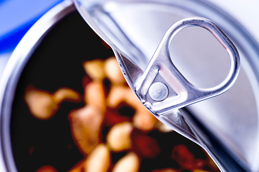 Opened metal can with lift tab and plastic lid containing mixed nuts on white background