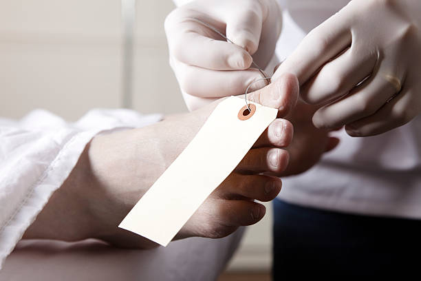 Toe Tag in the Morgue A close-up of the foot of a dead person in a morgue as the technician puts on a toe tag. morgue stock pictures, royalty-free photos & images