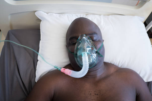 Patient lies in hospital bed on a respirator A senior African male patient lies in his hospital bed on a respirator medical ventilator photos stock pictures, royalty-free photos & images