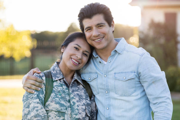 Couple smile for camera after wife's military tour reunion A mild adult couple stand in their front yard and embrace as they smile for the camera.  The wife is in military camo and has just returned from a tour. husband stock pictures, royalty-free photos & images