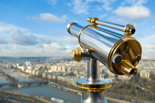 Old red binoculars stands at the edge of a cliff as it looks out toward a big river Danube and city in  Europe. Great view.