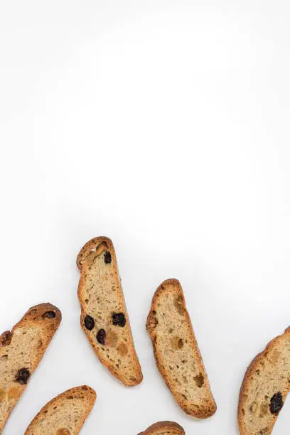 six long pieces of bright yellow and orange biscotti with white and black sultanas and nuts, dried sweet crispy italian bread/ On the lower part of vertical shot on the white background with copy space