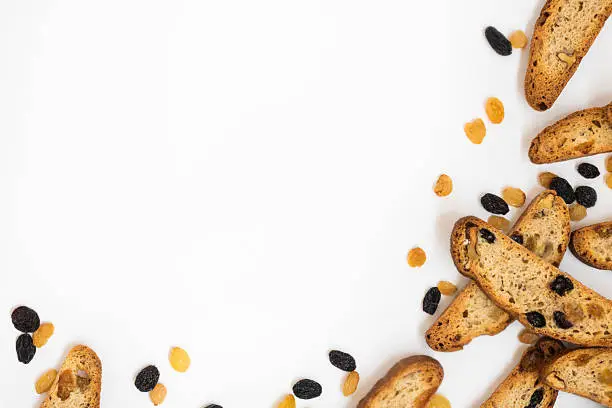 many long pieces of bright yellow and orange biscotti with white and black sultanas and nuts, dried sweet crispy italian bread On the right part and lower of horizontal shot on the white background with copy space