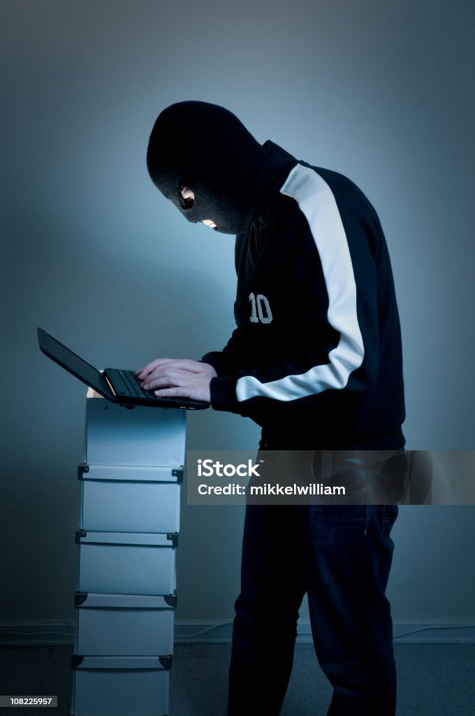 Hacker com máscara preto tipos de um laptop - Foto de stock de Adulto royalty-free