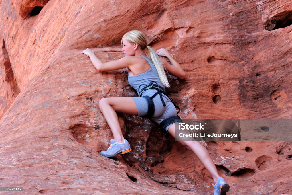 Young Woman Rock Climbing Attractive Blond Climbing Red Rock Of Southern Utah. Concept Image. Shoes have been altered & logos removed. Gripping Stock Photo