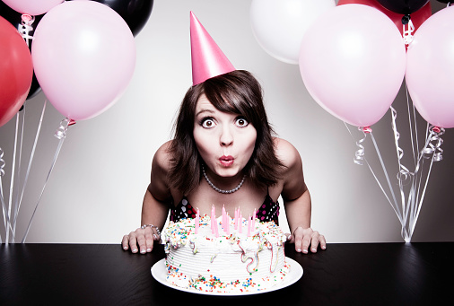Beautiful happy teen girl wearing black dress holding birthday cake with candle on a plate. Looking into the camera.