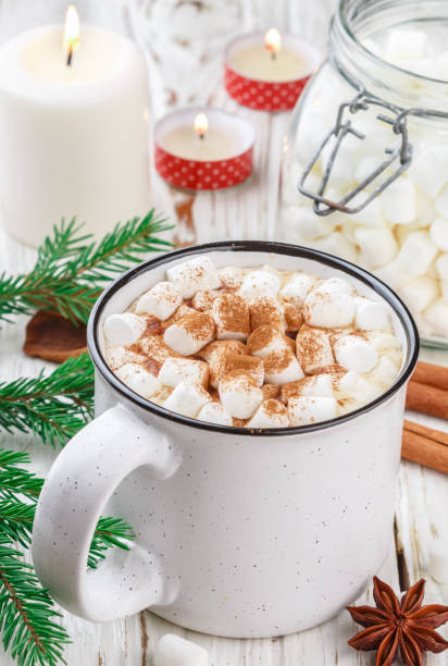istock Hot cocoa (coffee or chocolate) with marshmallows and cinnamon in a white Cup. Candy, candles and fir branches on the table. Christmas. New year. Rustic style. Selective focus 1082264596