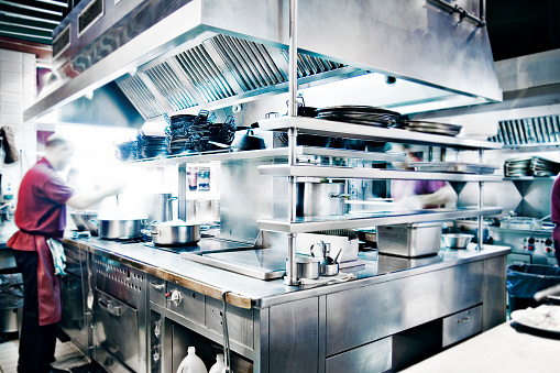 Cropped shot of waiter wiping the counter top in the kitchen with cloth. Man cleaning and maintaining commercial kitchen hygiene.