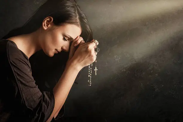 Young woman praying with rosary