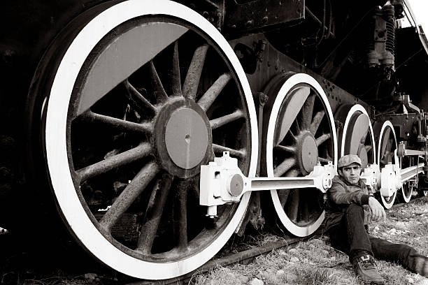 istock Young Man  Wearing Flat Cap Sitting By Steam Train Wheel 108226694