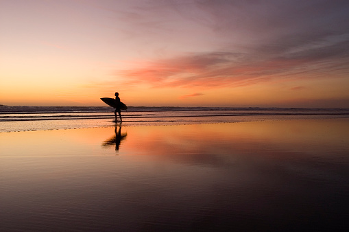 Lone surfer on beach at sunset