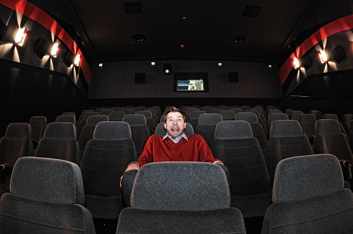 Scared man sitting in the movie theatre alone.