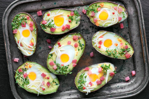 istock Keto diet dish: Avocado boats with ham cubes, quail eggs, cheese and cress sprouts on baking tray 1082292986