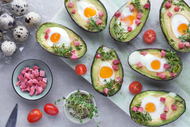 istock Keto diet dish: Avocado boats with quail eggs, ham cubes and cress sprouts on light stone serving board 1082294686
