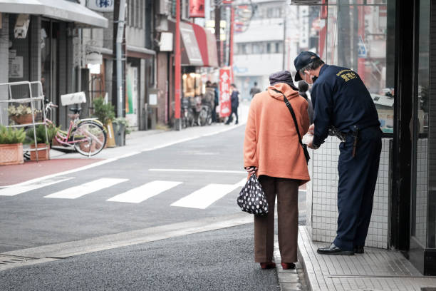 An old lady is asking direction and assistance from a local police on the street of japan. The policeman is wearing his uniform showing 'Policeman' on the back.