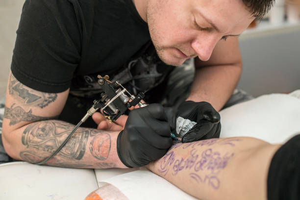 Tattooing Tattoo artist tattooing a male model. About 25 years old, Caucasian man. forearm tattoos men stock pictures, royalty-free photos & images