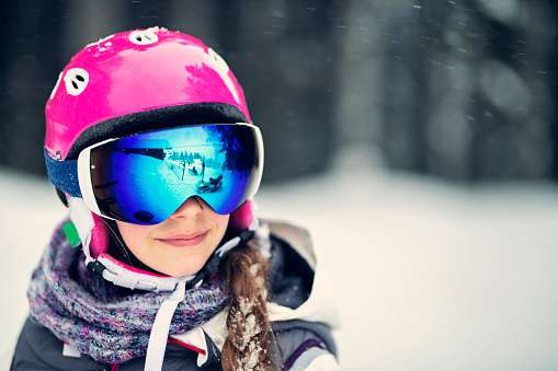 Happy little girl skiing on a beautiful winter day. Portrait of the girl wearing ski helmet.\nShot with Nikon D850