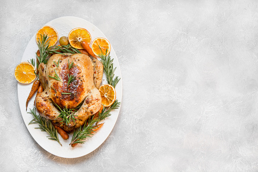 Traditional Christmas roasted chicken garnish orange, carrot, and rosemary on wooden table. Top view. Copy space.