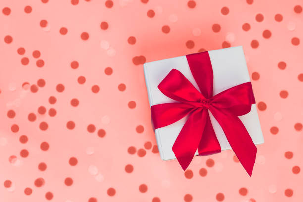 istock Gift box with red ribbon on coral background with round confetti. 1082331504